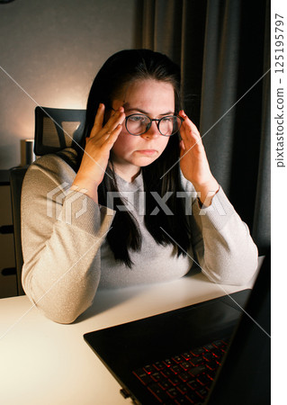 Woman working on computer late evening at home office. Concentrated female freelancer trying to solve business problems. Working and suffering from weariness. 125195797