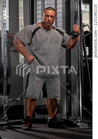 Elite fitness athlete showcasing impressive physique while preparing for a workout. The setting highlights a well equipped gym with weightlifting equipment and ample lighting. 125196219