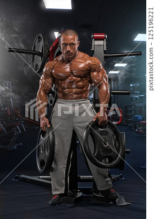 dedicated athlete lifts weights in a fitness gym showcasing impressive muscular definition and commitment to body sculpting. The atmosphere is energetic and motivating. 125196221
