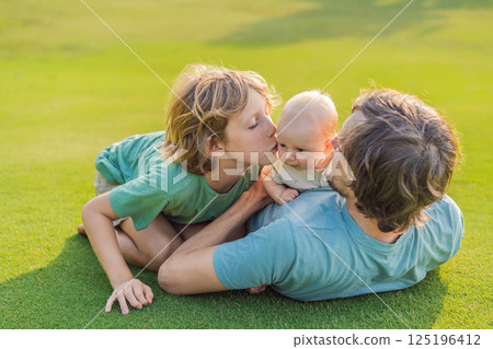 Father, older son, and newborn baby on a meadow in the park. Family spending quality time together in nature. Parenthood, love, and family bond concept 125196412