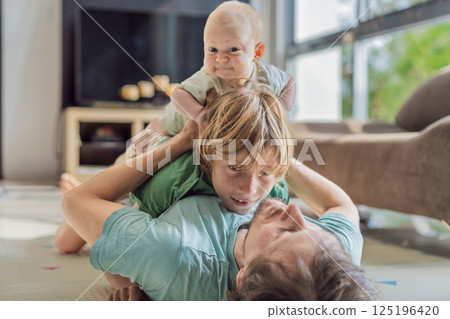 Father, son, and newborn baby lying on the floor in a cozy nursery, celebrating the arrival of their newest family member. Parenthood, bonding, and family love concept Father, son, and newborn baby lying on the floor in a cozy nursery, celebrating the arrival of their newest family member. Parenthood, bonding, and family love concept 125196420