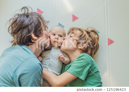 Father, son, and newborn baby lying on the floor in a cozy nursery, celebrating the arrival of their newest family member. Parenthood, bonding, and family love concept 125196423