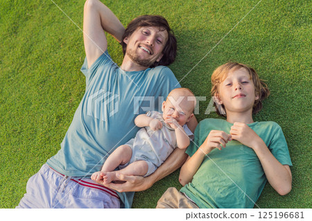 Father, older son, and newborn baby on a meadow in the park. Family spending quality time together in nature. Parenthood, love, and family bond concept 125196681