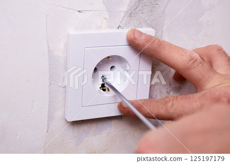 A person is using a screwdriver to install an electrical outlet on a white wall. 125197179