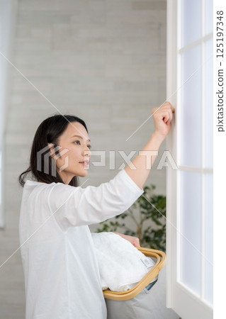 Woman holding a laundry basket and looking outside through an open window | Healthy living image | Well-being girl | Well-being Woman holding a laundry basket and looking outside through an open window | Healthy living image | Well-being girl | Well-being 125197348