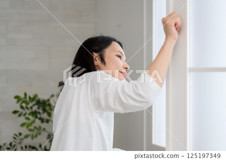 Woman looking outside from a bright room | Opening the window | Healthy living image | Well-being girl | Well-being 125197349
