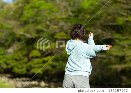 A middle-aged woman doing exercises by the riverside in the fresh greenery 125197952