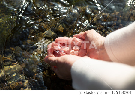 The hands of a middle-aged woman scooping clean river water 125198701