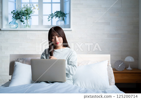一位年輕女子在床上操作電腦 一位年輕女子在床上操作電腦 125200714