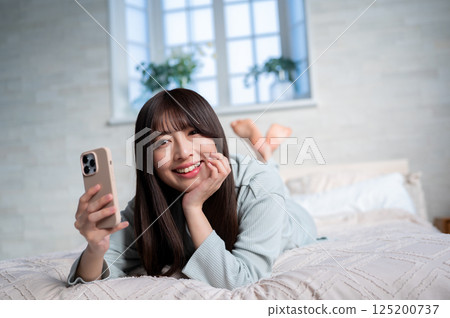 一名年輕女子麵朝下躺著，手裡拿著一支智慧型手機 125200737