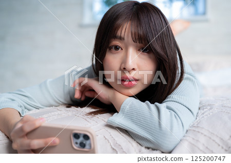 A young woman lying face down with a smartphone 125200747