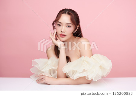 A beautiful young Asian woman with clean, fresh skin against a pink background. Skincare, facial treatment, cosmetology, beauty, and spa. An elegant portrait of an Asian woman. 125200883