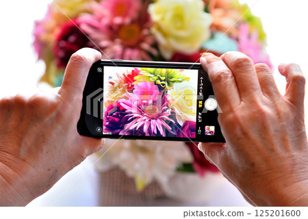 Senior taking photos of flowers with a mobile phone 125201600
