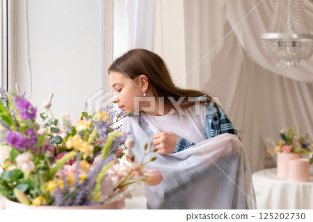 Girl smelling flowers near window with closed eyes indoors. 125202730