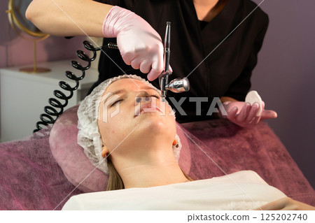 Professional applies microdermabrasion airbrush treatment to client's face 125202740