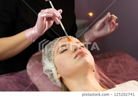 Esthetician brushes hydrating facial mask onto client's forehead in spa Esthetician brushes hydrating facial mask onto client's forehead in spa 125202741