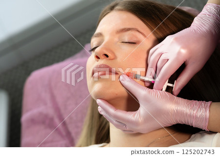 Professional administers lip filler injection into patient's cheek 125202743