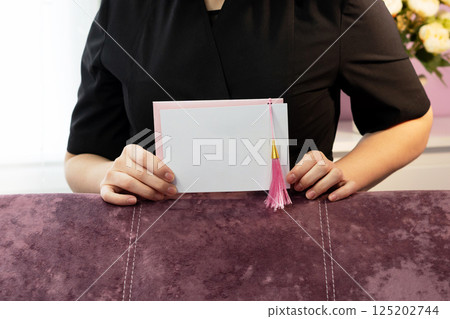 Person displaying blank greeting card with pink tassel. 125202744