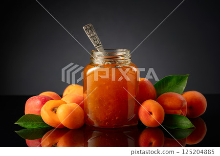 Apricot jam in glass jar and fresh fruits on a black reflective background. 125204885
