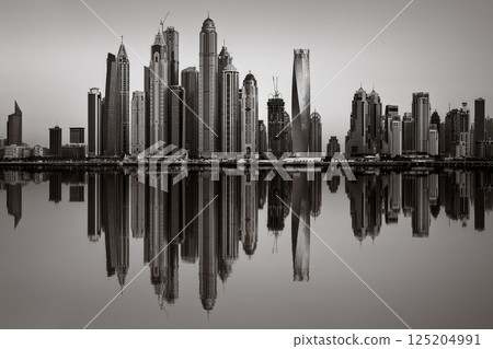 Monochrome city skyline with tall skyscrapers reflecting on calm water under a cloudy sky, Dubai Marina bay UAE Monochrome city skyline with tall skyscrapers reflecting on calm water under a cloudy sky, Dubai Marina bay UAE 125204991