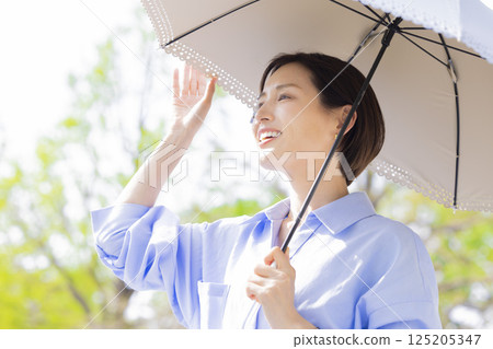 UV care: A woman walking with a parasol among the fresh greenery 125205347