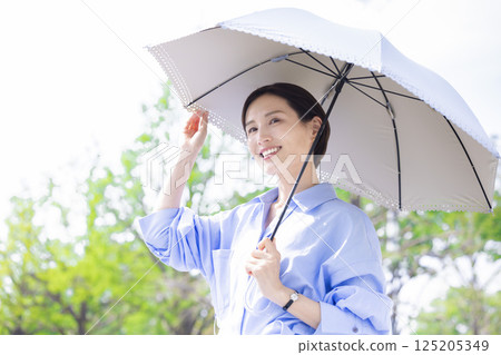 UV care: A woman walking with a parasol among the fresh greenery 125205349
