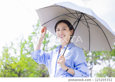 UV care: A woman walking with a parasol among the fresh greenery UV care: A woman walking with a parasol among the fresh greenery 125205352