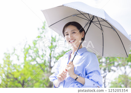 UV care: A woman walking with a parasol among the fresh greenery 125205354