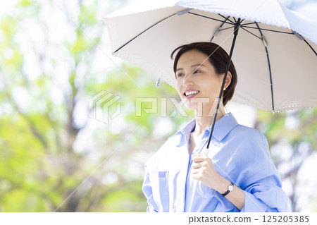 紫外線護理：一位女士撐著陽傘在綠樹叢中漫步 125205385