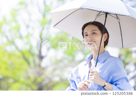 UV care: A woman walking with a parasol among the fresh greenery 125205386