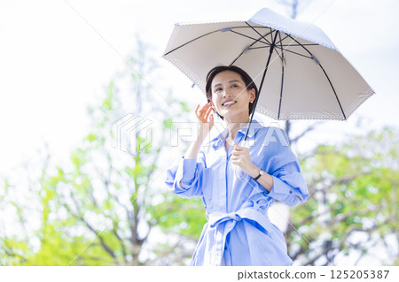 UV care: A woman walking with a parasol among the fresh greenery 125205387