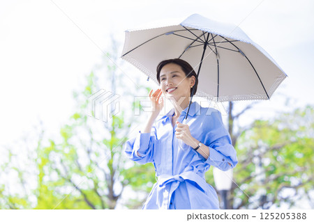 UV care: A woman walking with a parasol among the fresh greenery 125205388