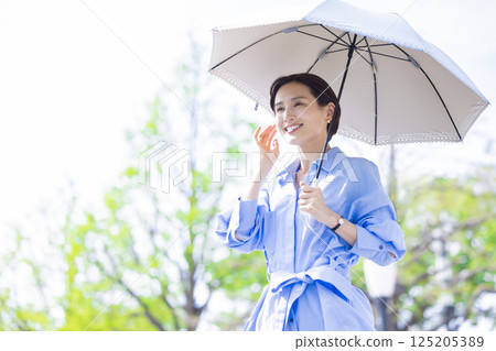 UV care: A woman walking with a parasol among the fresh greenery 125205389