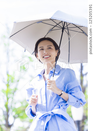 UV care: A woman walking with a parasol among the fresh greenery 125205391