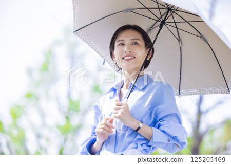 紫外線護理：一位女士撐著陽傘在綠樹叢中漫步 125205469