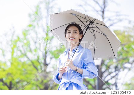 紫外線護理：一位女士撐著陽傘在綠樹叢中漫步 125205470