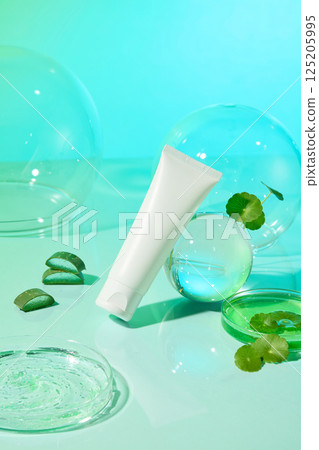 Vertical photo of a cream tube tilted, placed next to a glass sphere. Petri dish filled with green liquid and fresh gotu kola leaves. Aloe vera cut into pieces and stacked on top of each other. Vertical photo of a cream tube tilted, placed next to a glass sphere. Petri dish filled with green liquid and fresh gotu kola leaves. Aloe vera cut into pieces and stacked on top of each other. 125205995