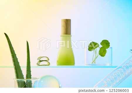 Essence bottle with wooden lid, aloe vera cut into pieces and pennywort plants placed in beaker, both display on glass surface. Aloe vera plant with thorns along the stem, placed in measuring cup. 125206003