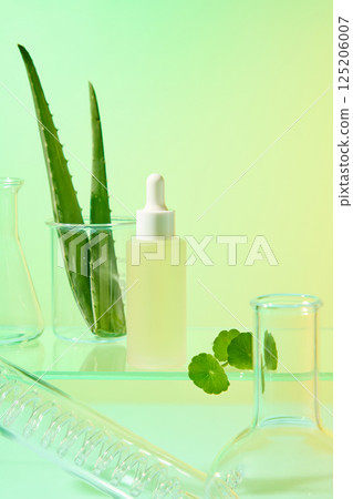 Dropper serum bottle containing essence from natural ingredients. Fresh aloe vera with thorns, fresh gotu kola leaves presented on the glass surface. Florence flask and conical flask placed around Dropper serum bottle containing essence from natural ingredients. Fresh aloe vera with thorns, fresh gotu kola leaves presented on the glass surface. Florence flask and conical flask placed around 125206007