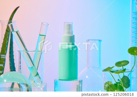 A spray bottle with a turquoise packaging stands on a glass pedestal. Test tubes placed in measuring cups. Fresh aloe vera plants have long stems, Centella has soft stems and round leaves.  125206018