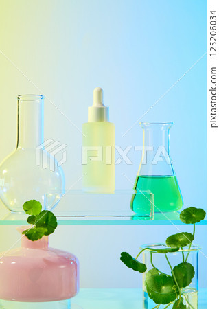 Dropper serum bottles placed on a glass podium, behind are Florence flask and conical flask containing green liquid. The essence extracted from natural pennywort is green. Vase with centella plants. 125206034