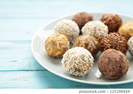 Healthy raw energy balls. Candy vegan balls of dates, nuts and coconut on plate on blue background. Top view, concept of useful home-made candies without sugar 125206884