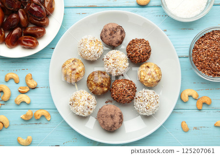 Healthy raw energy balls. Candy vegan balls of dates, nuts and coconut on plate on blue background. Top view, concept of useful home-made candies without sugar Healthy raw energy balls. Candy vegan balls of dates, nuts and coconut on plate on blue background. Top view, concept of useful home-made candies without sugar 125207061
