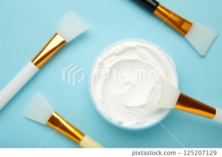 Cosmetic mask (scrub) in a bowl with brush on blue background. 125207129