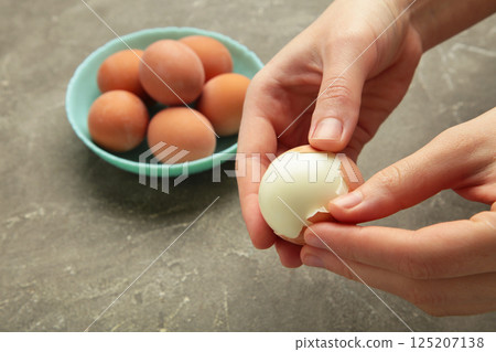 Woman peeling boiled egg on grey background, closeup 125207138