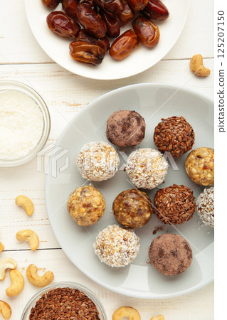 Healthy raw energy balls. Candy vegan balls of dates, nuts and coconut on plate on white background. Top view, concept of useful home-made candies without sugar. Vertical photo 125207150