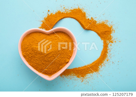 Healthy turmeric powder in a white heart shaped bowl on blue background. 125207179