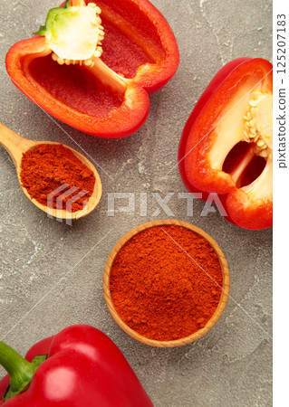 Paprika powder with fresh red pepper on grey background. Vertical photo Paprika powder with fresh red pepper on grey background. Vertical photo 125207183