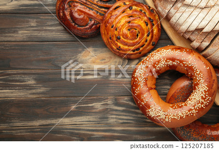 Bakery - various kinds of breadstuff. Bread rolls, bagel, sweet bun on brown wooden background. Space for text 125207185