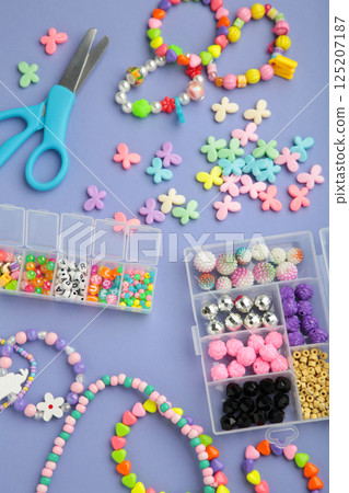 Box with beads to create hand made jewelry for child on violet background. Making bracelet. Handmade accessories. Vertical photo Box with beads to create hand made jewelry for child on violet background. Making bracelet. Handmade accessories. Vertical photo 125207187